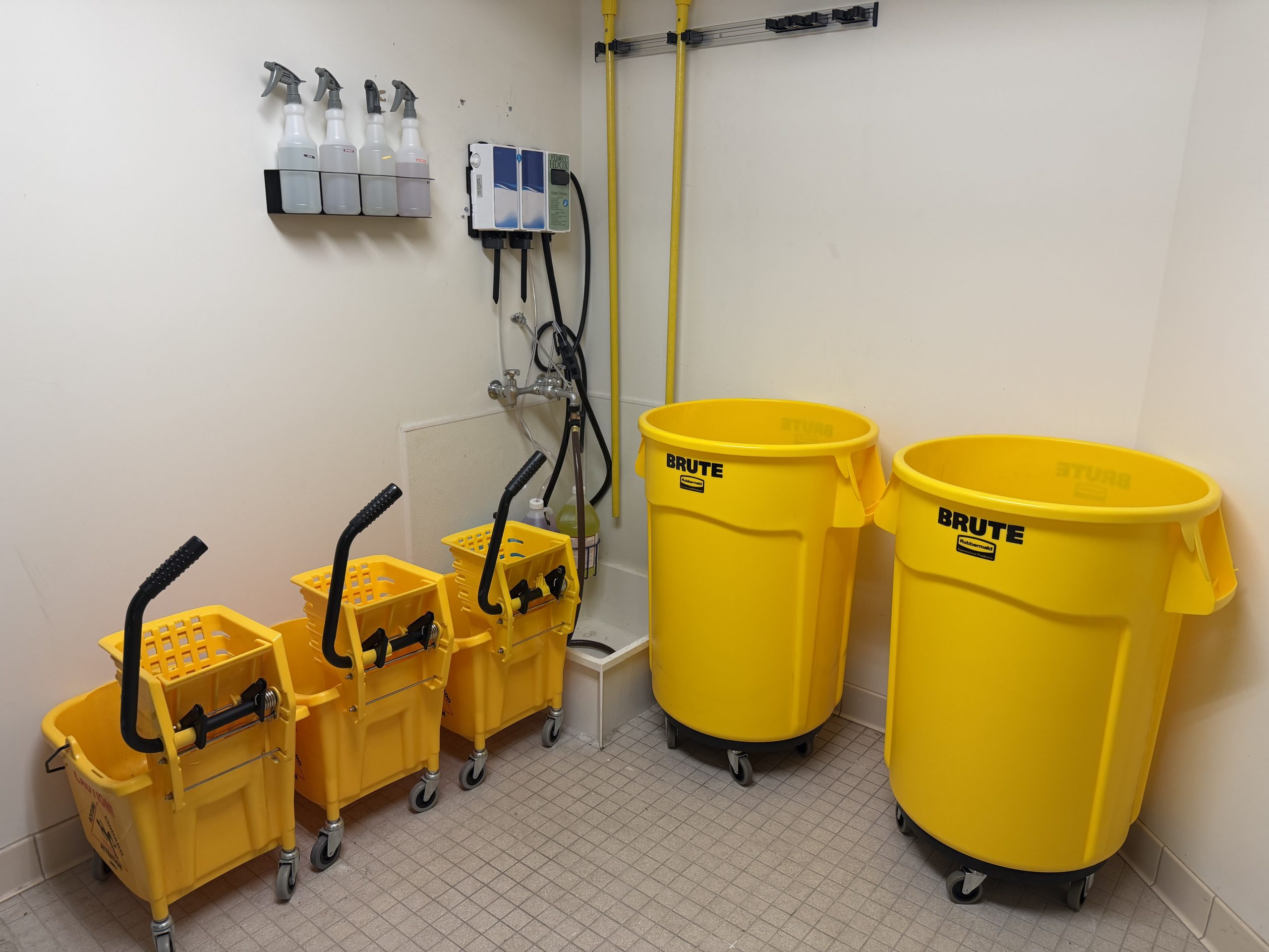 Organized janitor's closet with mop buckets, waste bins and dispensing station