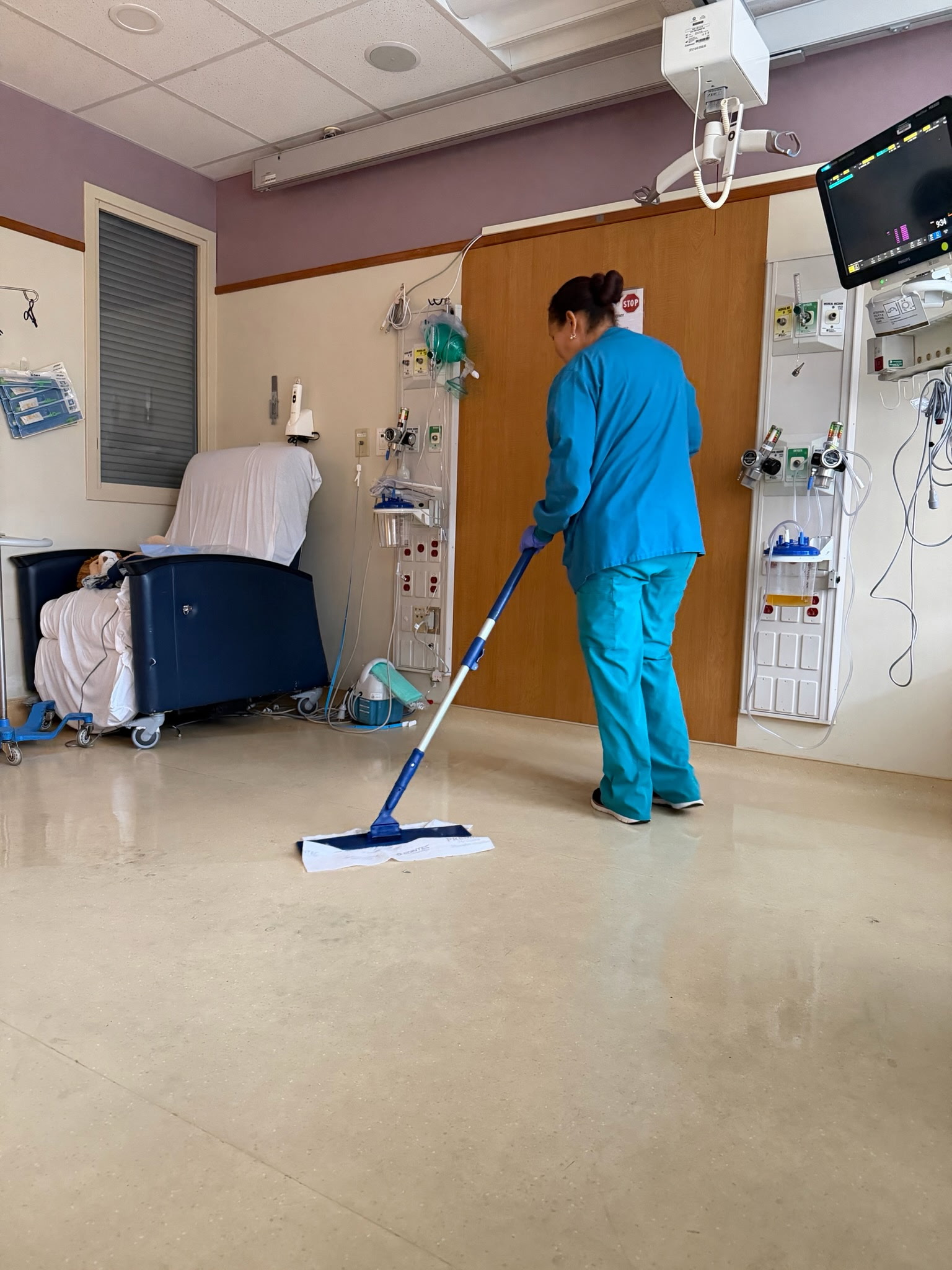 Team member in scrubs mopping a hospital patient room